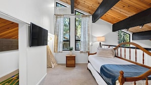 Quarto com cama, mesa de cabeceira, TV fixada na parede e janela com cortinas.