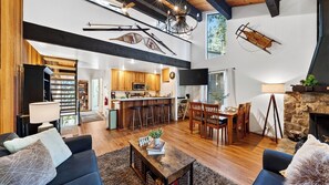 A spacious living area with a fireplace, a kitchen with wooden cabinets, and a dining area with a high ceiling and exposed beams.