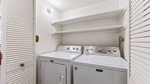 Une buanderie équipée de deux machines à laver et de deux sèche-linge Maytag, une porte blanche avec un trou de serrure et une étagère au-dessus des sèche-linge.