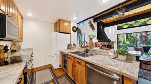 A modern kitchen with wooden cabinets, a built-in oven, a sink, and a stone fireplace. - Tahoe Pines Retreat by Avantstay Pool + Sauna + Pickleball Access Bunk Room Near Lake + Skiing (Kings Beach)