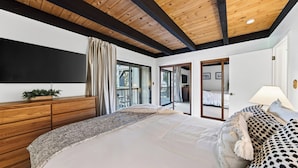 Quarto com cama grande, penteadeira de madeira, espelho e vista para um deck externo.