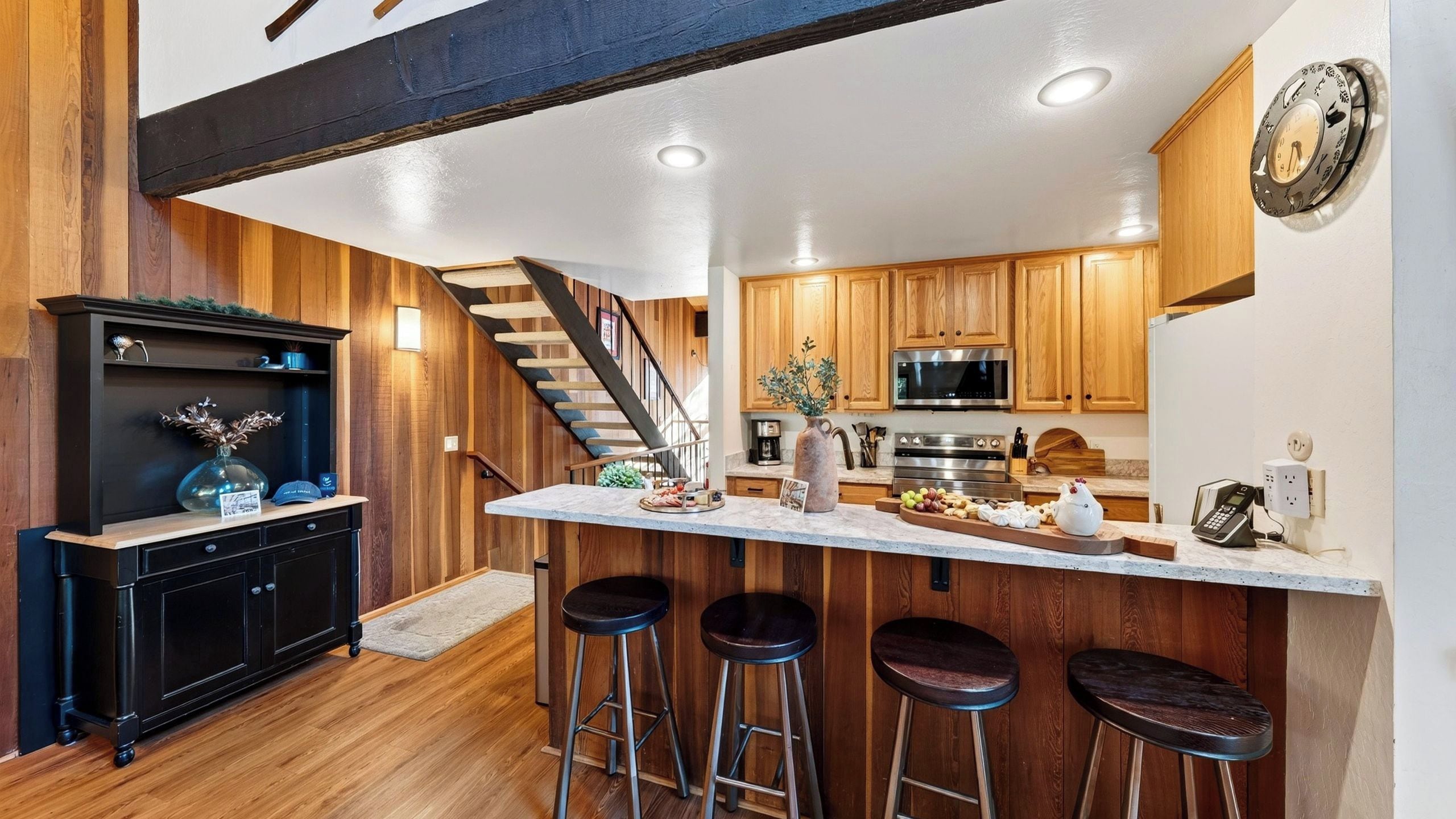 A modern kitchen with wooden cabinets, a stainless steel refrigerator, and a bar area with stools.