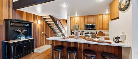 A modern kitchen with wooden cabinets, a stainless steel refrigerator, and a bar area with stools.