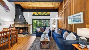 A cozy living room with a fireplace, wooden furniture, and a view of the outdoors.