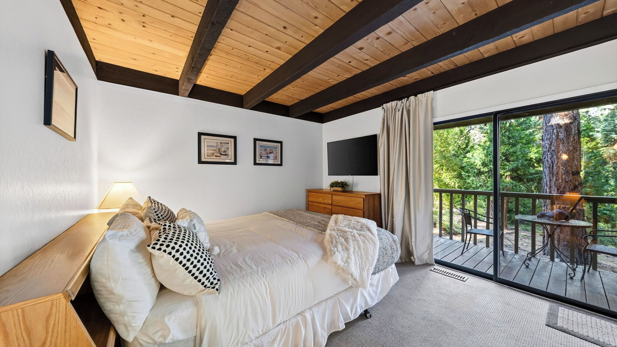 A bedroom with a bed, a dresser, a TV, and a balcony with outdoor furniture.