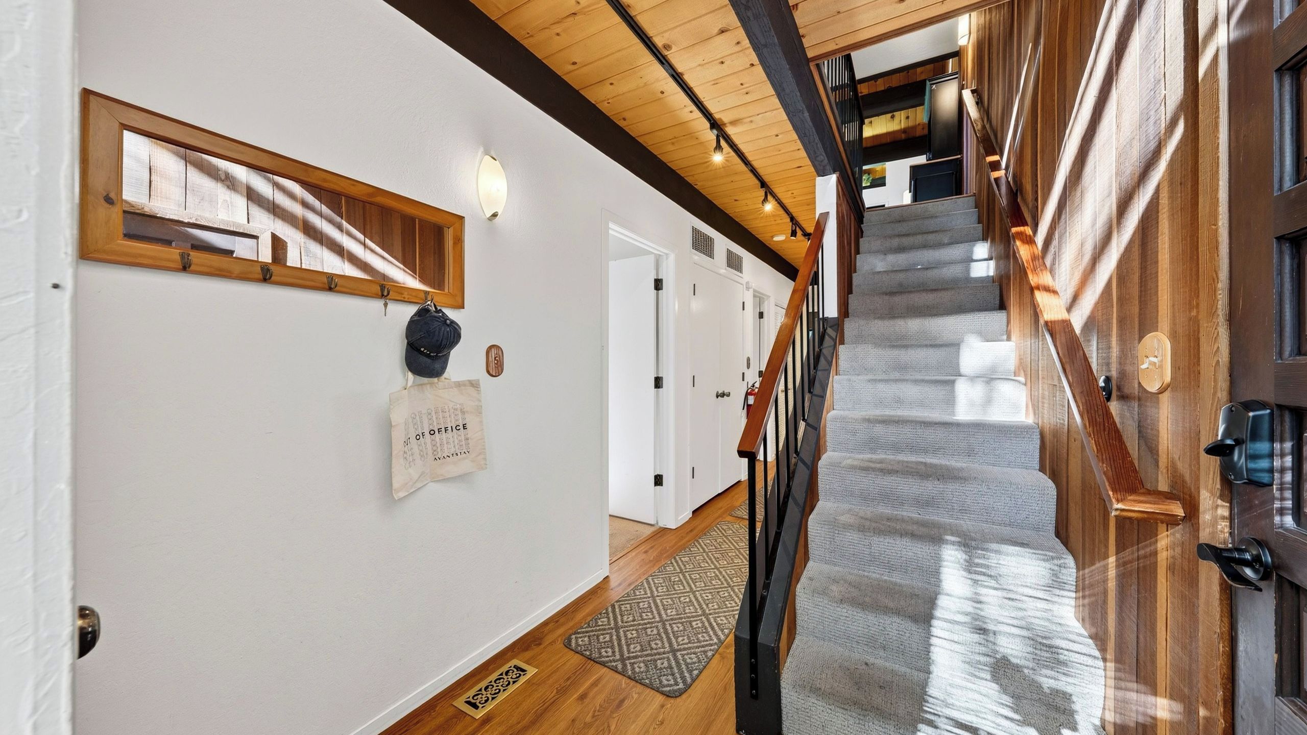 A hallway with a wooden staircase, a coat rack, and a sign on the wall.