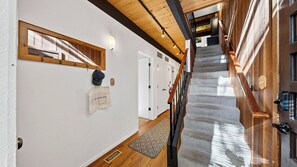 A hallway with a wooden staircase, a coat rack, and a sign on the wall. - Tahoe Pines Retreat by Avantstay Pool + Sauna + Pickleball Access Bunk Room Near Lake + Skiing (Kings Beach)