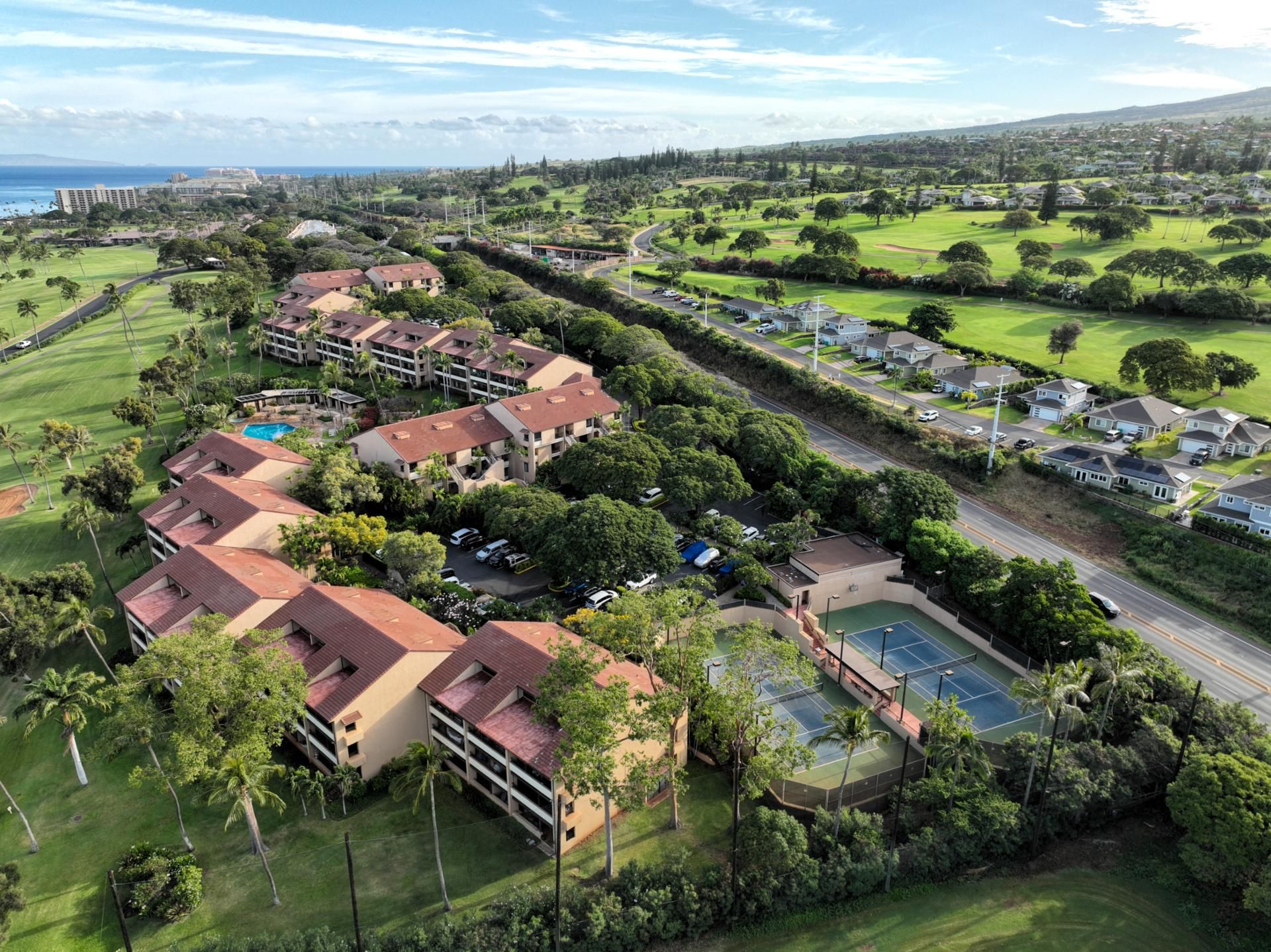 A golf course with a tennis court, surrounded by residential buildings and lush greenery.