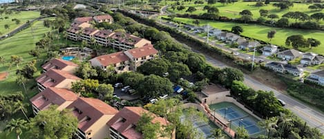 A golf course with a tennis court, surrounded by residential buildings and lush greenery.