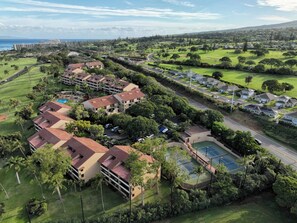 Luchtbeeld van een resort met meerdere gebouwen, een tennisbaan en weelderige begroeiing.