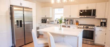 Een moderne keuken met roestvrijstalen apparatuur, witte kasten en een centraal eiland met zitplaatsen.