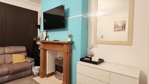 A living room with a fireplace, a sofa, a television, and a framed picture on the wall. - Ellie's Guest House (Whitby)