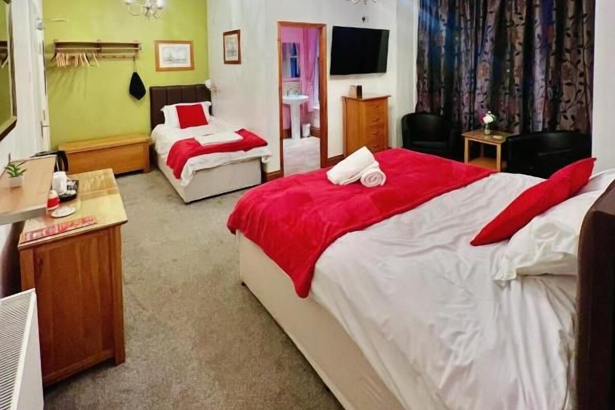 A hotel room with two beds, a desk, a chair, a TV, and a window with curtains.