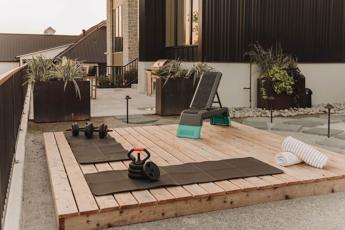 Un espace d’entraînement en plein air équipé de tapis de sol, d’haltères, d’un kettlebell et d’un banc.