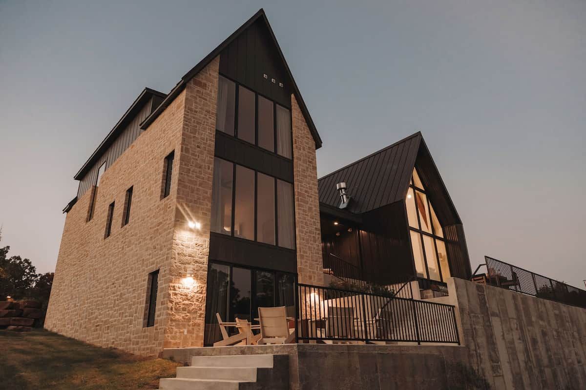 A modern two-story building with a stone facade, large windows, and a balcony with outdoor seating.
