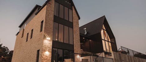 A modern two-story building with a stone facade, large windows, and a balcony with outdoor seating.