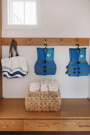 A room with a wooden bench, a woven basket, and three blue life jackets hanging on a wooden rack. - Lakefront Retreat | The Lucas (Eufaula)