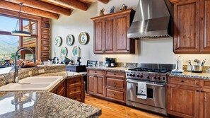 A kitchen with granite countertops, wooden cabinets, stainless steel appliances, and a view of the mountains. - 115 Tristant by Avantstay Hot Tub + Gym + Ridge Views Ski-in/out Funicular + Gondola (Telluride)
