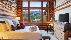 Ein Schlafzimmer in einer Blockhütte mit einem Bett, Kissen, einem Schreibtisch, einem Sessel, einer Kommode und einem Fernseher.