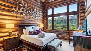 A log cabin-style bedroom with a large bed, wooden headboard, and a view of mountains through large windows. - 115 Tristant by Avantstay Hot Tub + Gym + Ridge Views Ski-in/out Funicular + Gondola (Telluride)