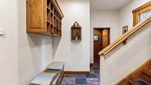 A hallway with a wooden staircase, a bench, a wall-mounted shelf with a picture, and a door leading to another room. - 115 Tristant by Avantstay Hot Tub + Gym + Ridge Views Ski-in/out Funicular + Gondola (Telluride)