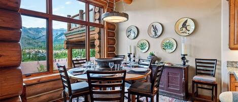A dining area with a wooden table and chairs, a view of mountains, and decorative plates on the wall.