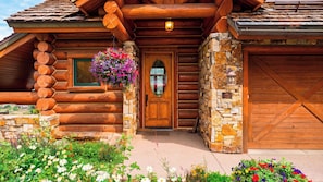 A log cabin with a stone foundation, a wooden front door, and a hanging flower basket. - 115 Tristant by Avantstay Hot Tub + Gym + Ridge Views Ski-in/out Funicular + Gondola (Telluride)