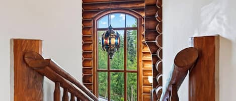 Un escalier en bois offrant une vue sur une forêt, visible à travers une grande fenêtre en arc de cercle.