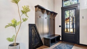 A modern entryway with a dark door, a bench, and a wall-mounted coat rack. - The Blackwood A-frame by Avantstay Hot Tub & Pond Arcade Room EV Charger Near Slopes & Lake (Big Bear Lake)