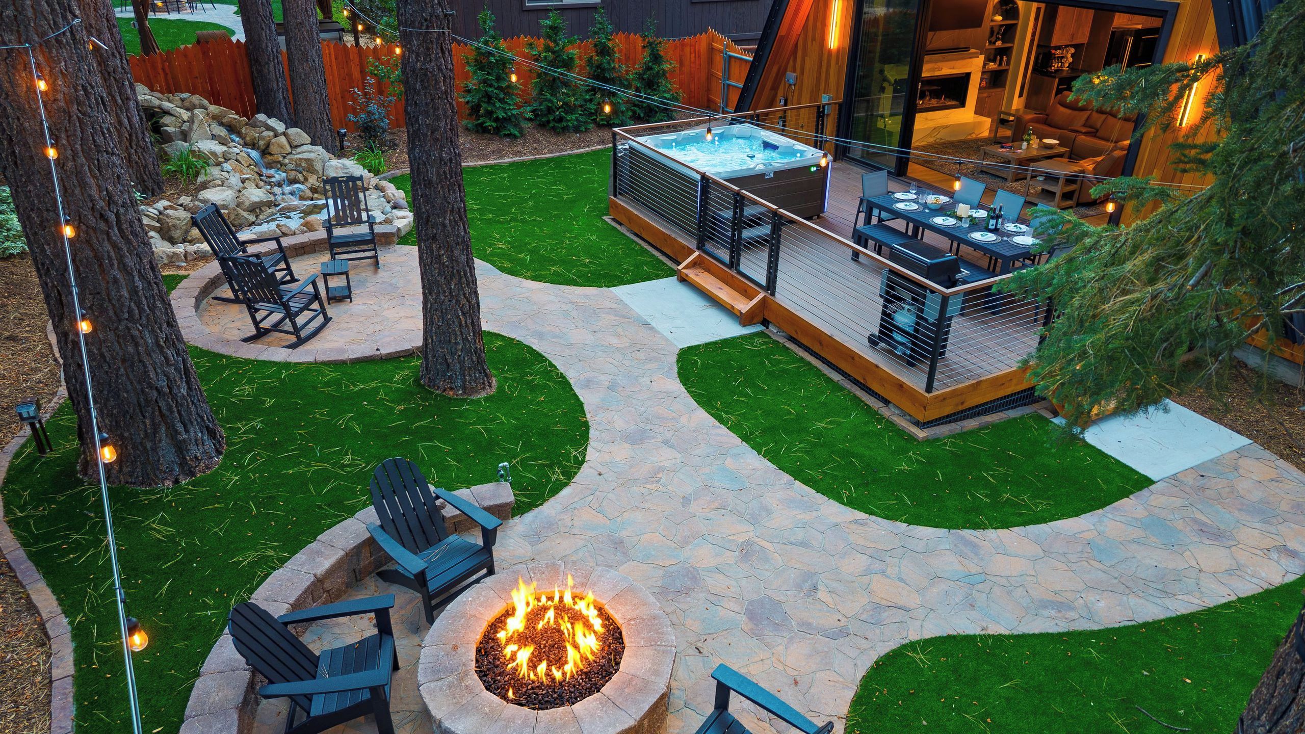 A backyard with a hot tub, outdoor seating, a fire pit, and a stone patio.