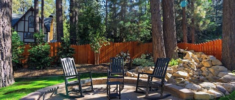 A patio area with stone flooring, wooden chairs, a wooden fence, and a pile of rocks.