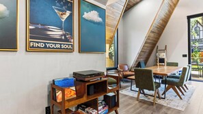 A modern living room with a wooden coffee table, a bookshelf, and a dining area with chairs. - The Blackwood A-frame by Avantstay Hot Tub & Pond Arcade Room EV Charger Near Slopes & Lake (Big Bear Lake)