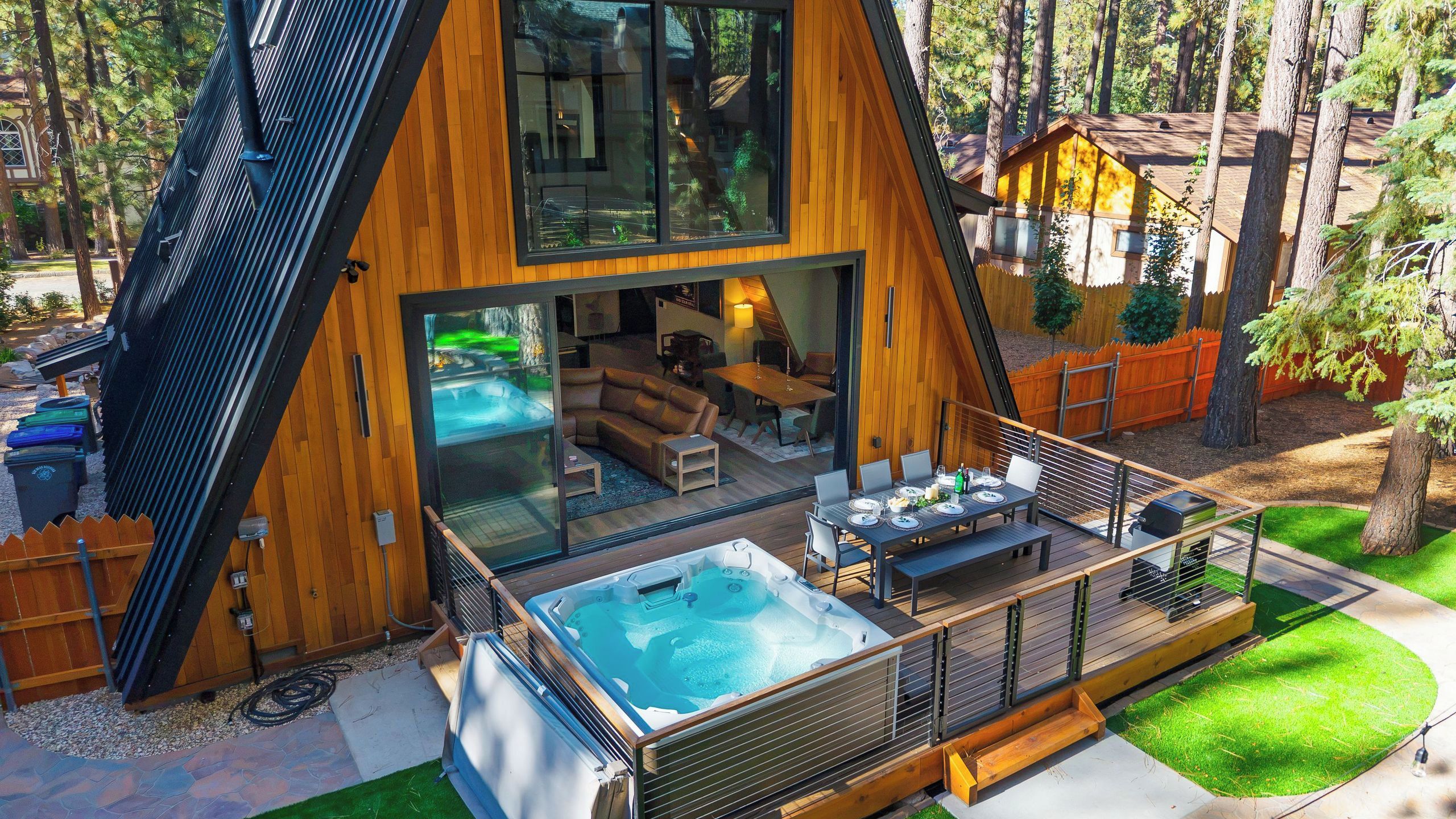 A modern A-frame cabin with a hot tub, outdoor seating, and a deck.