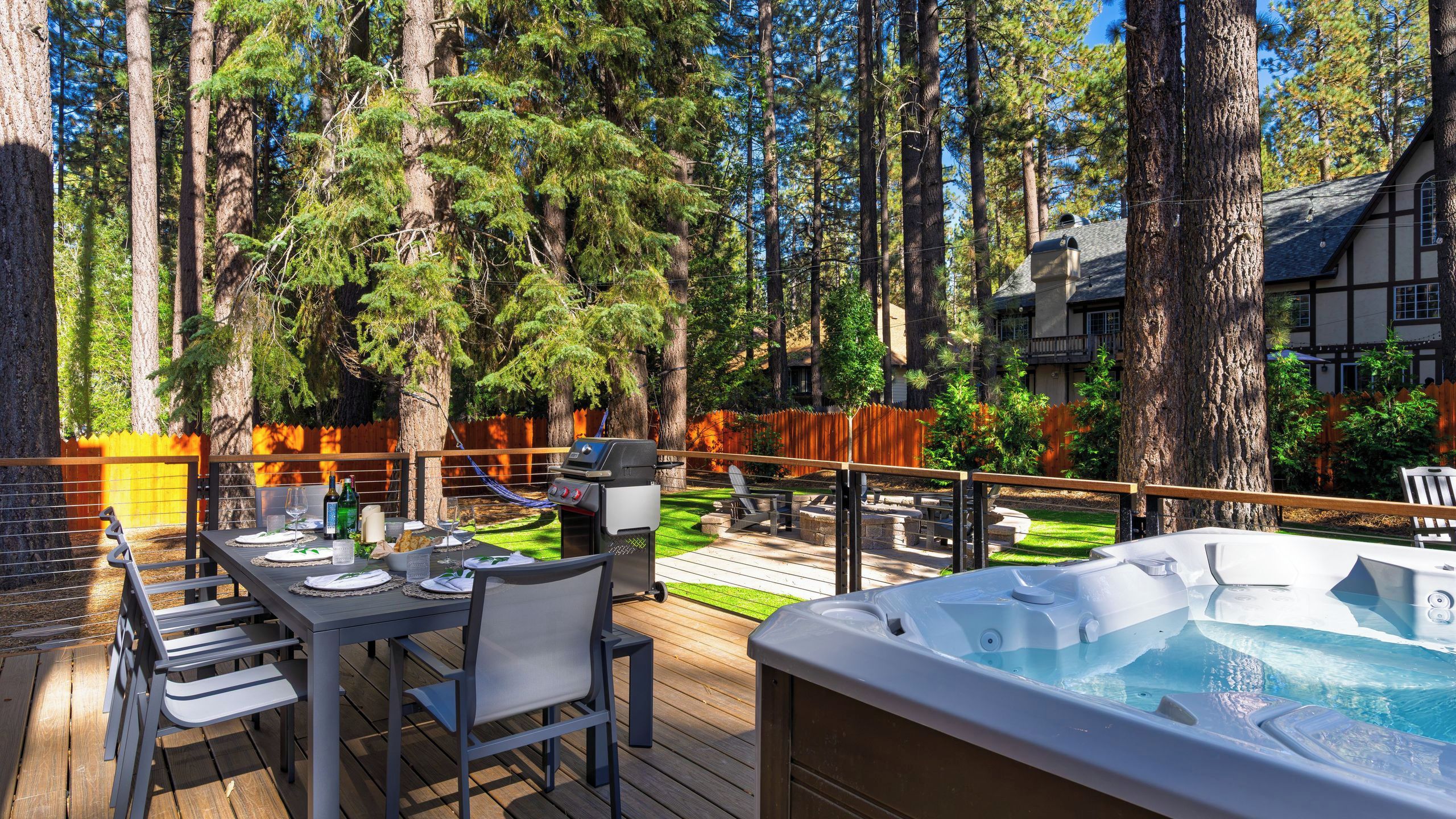 A deck with a hot tub, dining table, and chairs, surrounded by trees.