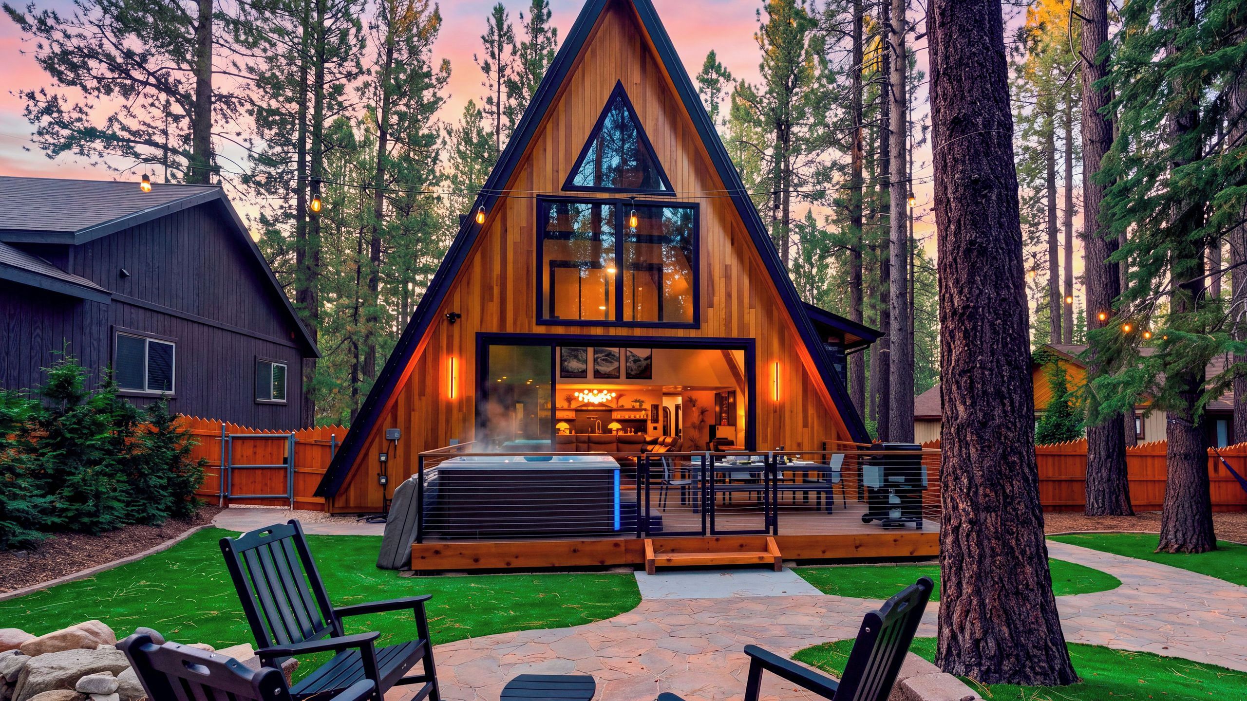 A modern A-frame lodge with a hot tub and outdoor seating area.