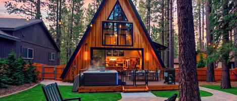 A modern A-frame lodge with a hot tub and outdoor seating area.