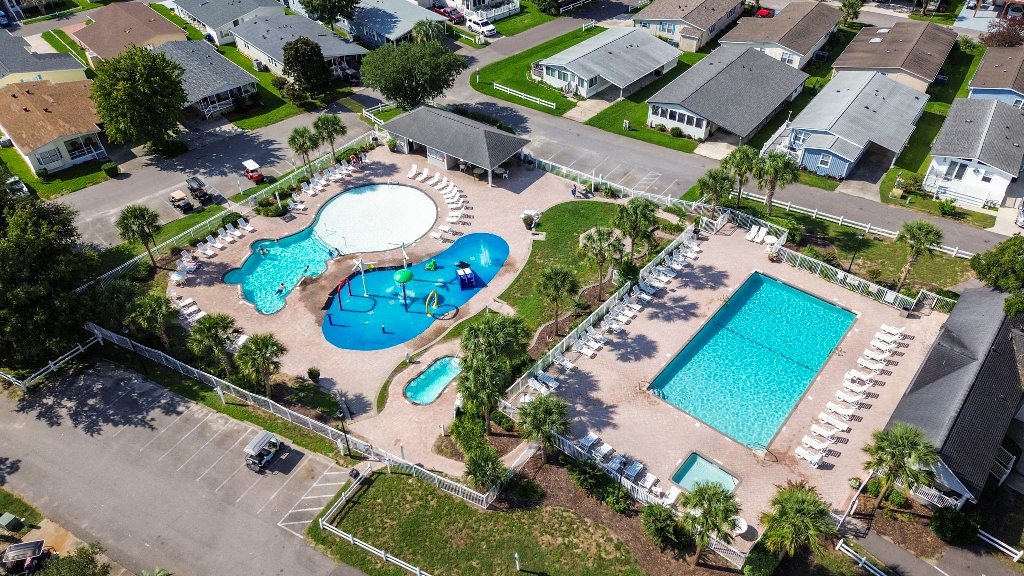 A residential area with a large swimming pool surrounded by lounge chairs and palm trees.