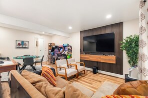 A modern living room with a flat-screen TV, comfortable seating, a pool table, and arcade games. - Designer 6BR in Massanutten with Hot Tub, Sauna (McGaheysville)