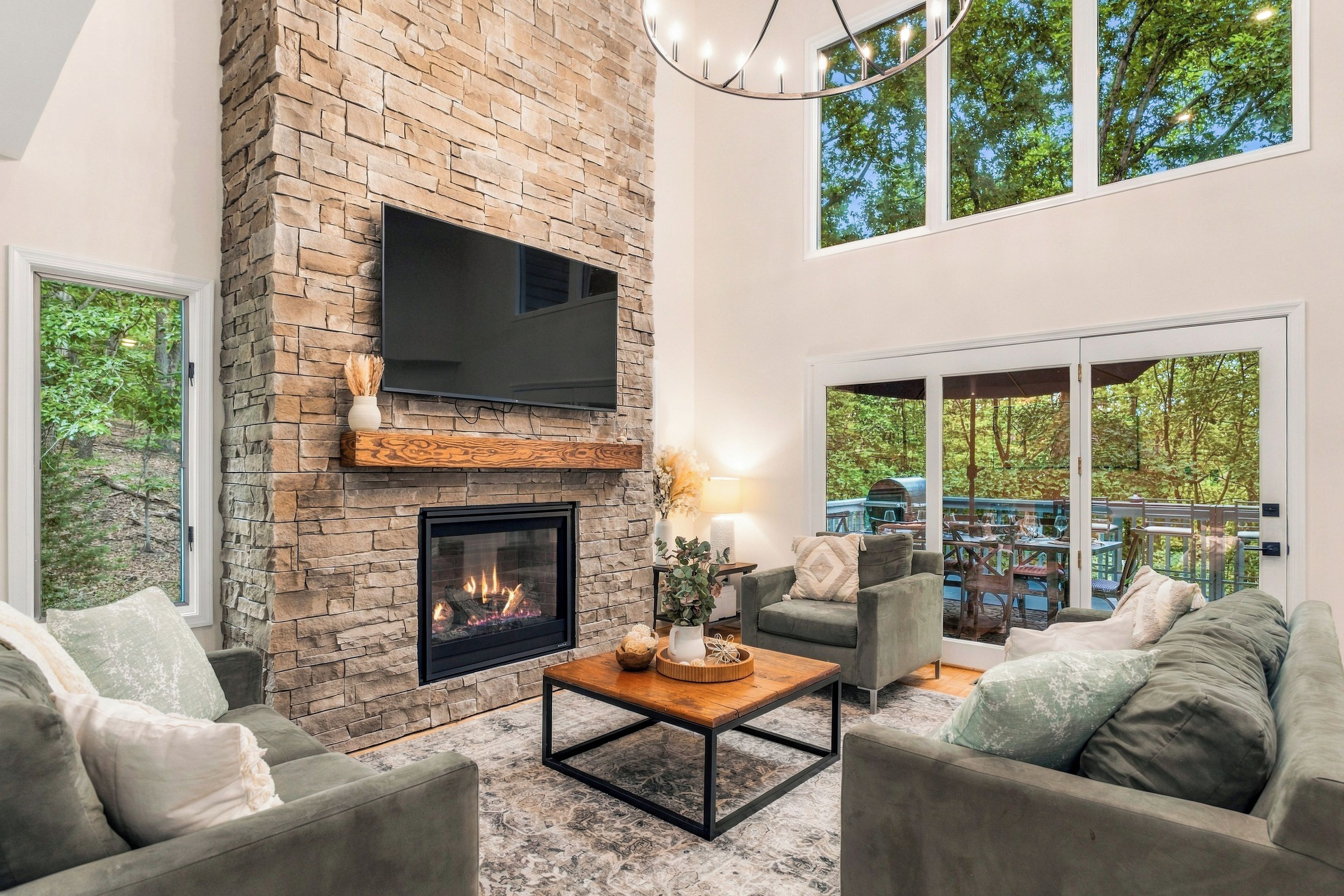 A modern living room with a stone fireplace, comfortable seating, and large windows offering a view of the outdoors.