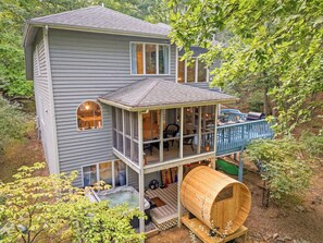 Uma casa de dois andares com hidromassagem, sauna em um barril de madeira e um deck com área de estar externa.