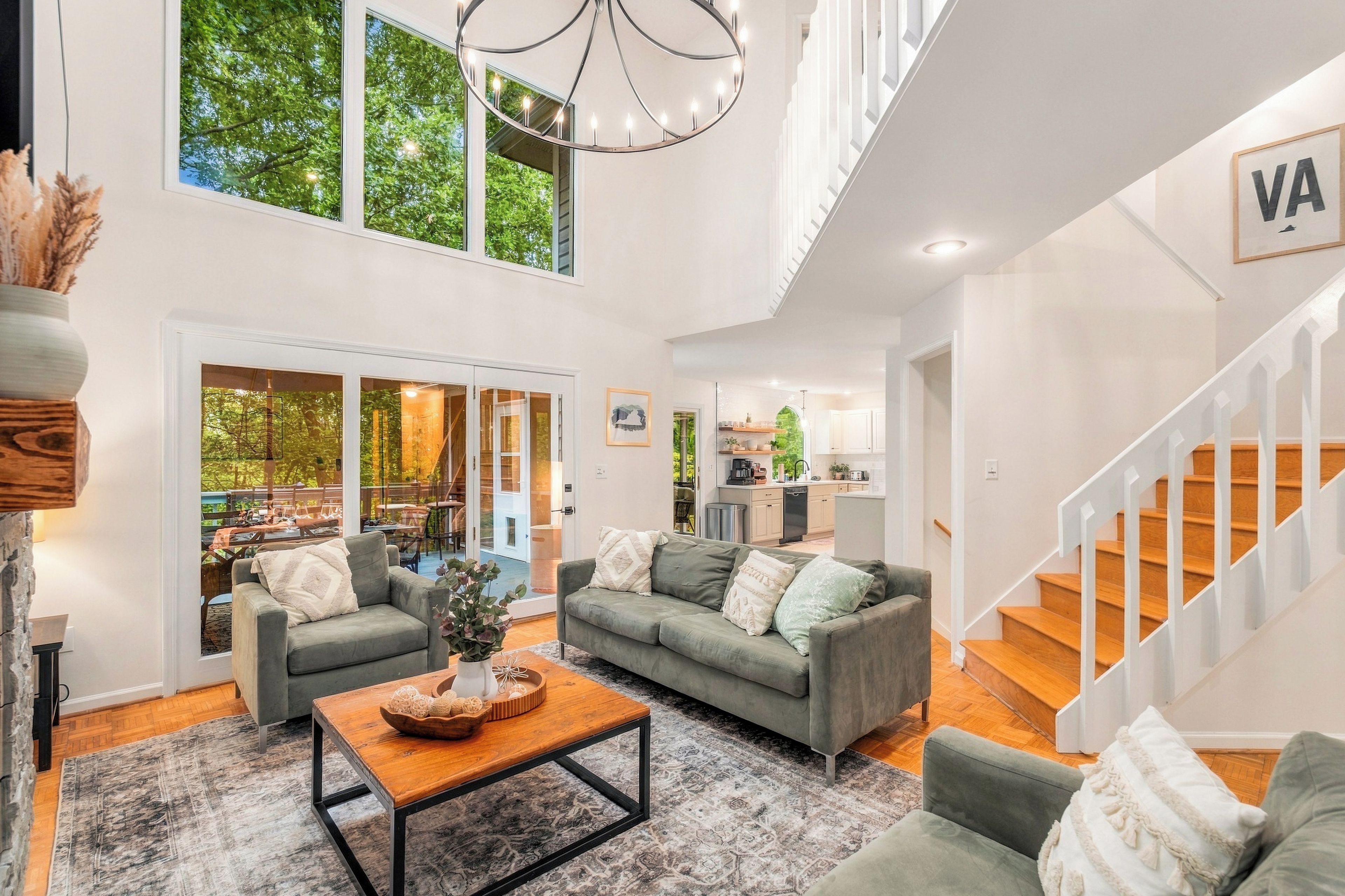 Amplia sala de estar con techo alto, una escalera y una cocina visible a través de una puerta abierta.