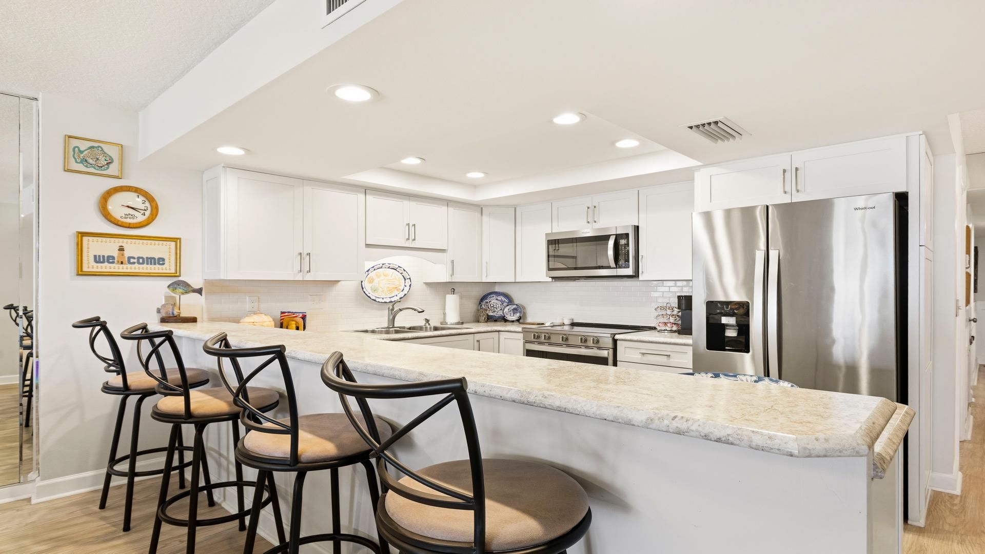 Une cuisine moderne avec des meubles blancs, un réfrigérateur en acier inoxydable et un coin bar équipé de tabourets.