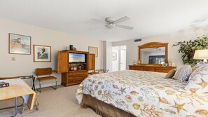 Ein Schlafzimmer mit einem Bett, einem Schreibtisch, einem Stuhl, einem Kleiderschrank, einem Deckenventilator und einem großen Spiegel.