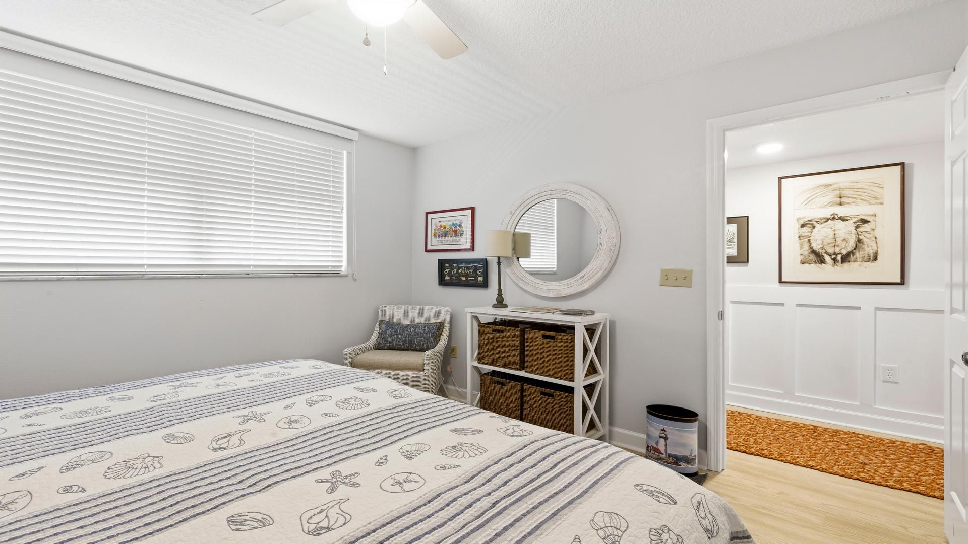 A bedroom with a bed, a chair, a bedside table with a lamp, a wall-mounted mirror, and framed artwork.