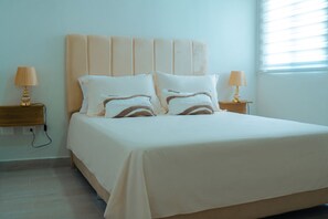 Ein ordentlich bezogenes Bett mit Kopfteil, zwei Nachttischlampen und einer Steckdose an der Wand.