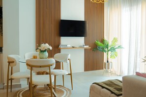 Ein modernes Wohnzimmer mit einem flachbildfernseher an der Wand, einem Esstisch mit Stühlen und einer Zimmerpflanze.