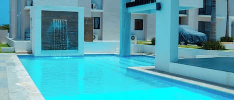 A modern hotel with a swimming pool, covered car, and a covered area with a water feature.