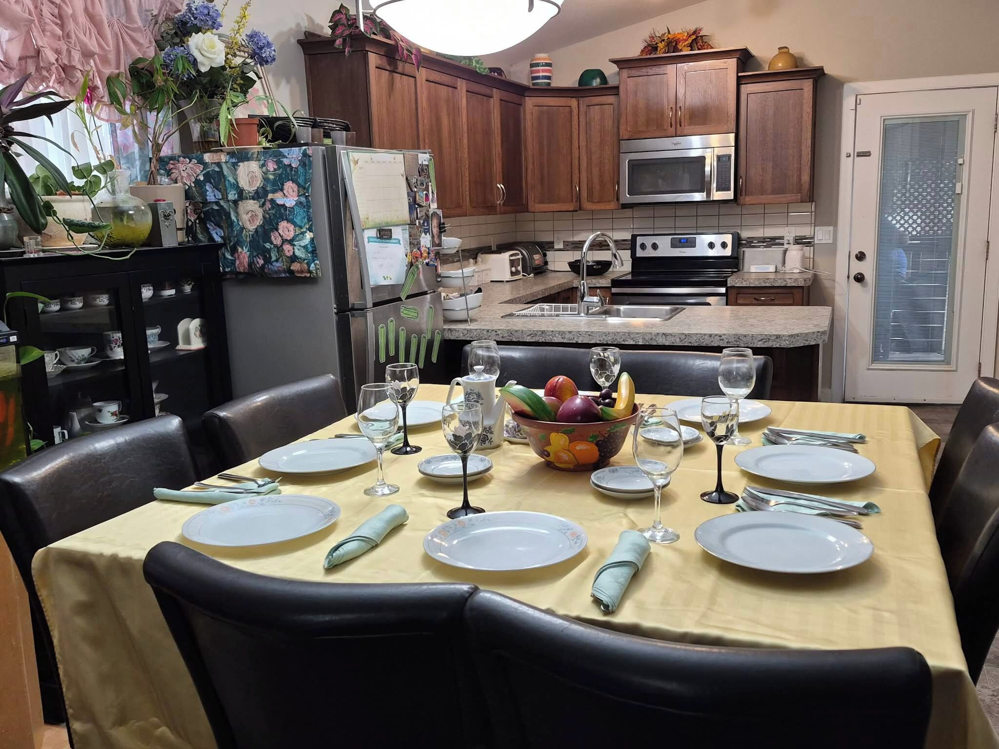 Comedor con una mesa dispuesta para seis personas, rodeada de sillas, en una cocina con armarios de madera y electrodomésticos modernos.
