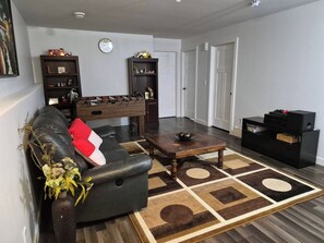 A living room with a sofa, a coffee table, a foosball table, and a bookshelf. - Home Sweet Home Away From Home (Red Deer)