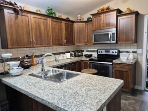 A kitchen with granite countertops, wooden cabinets, a stainless steel microwave, a toaster, and a dishwasher. - Home Sweet Home Away From Home (Red Deer)